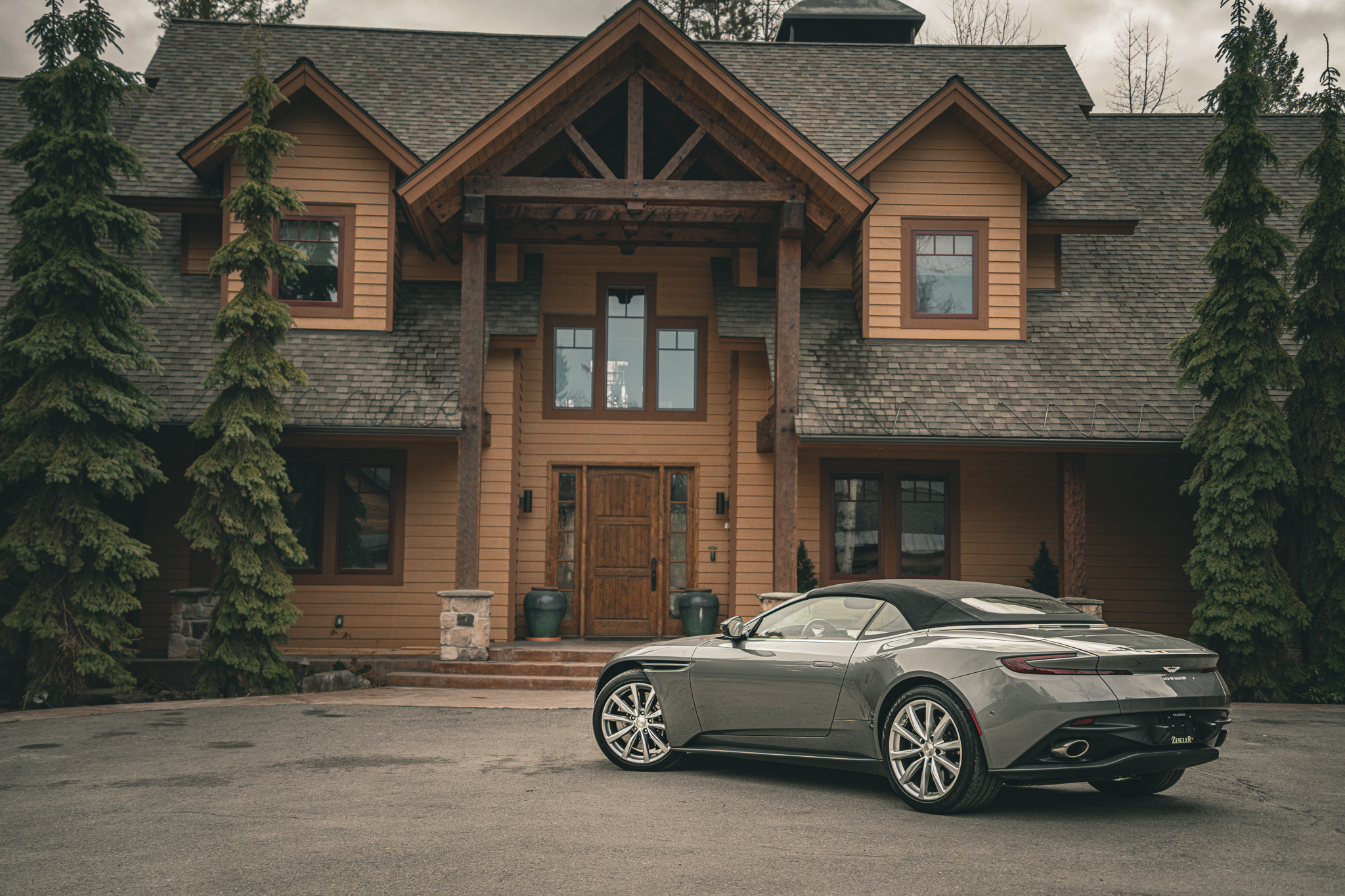 A silver Aston Martin photographed outside a timber home